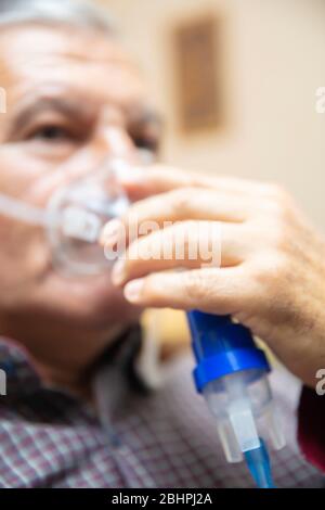 Senior man using medical equipment for inhalation with respiratory mask, nebulizer in the room Stock Photo