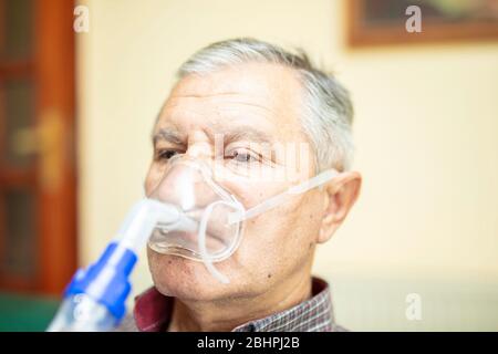 Senior man using medical equipment for inhalation with respiratory mask, nebulizer in the room Stock Photo