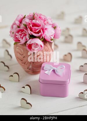 Beautiful composition with small square metallic pink gift box and delicate roses in pink vase on white wooden background Stock Photo