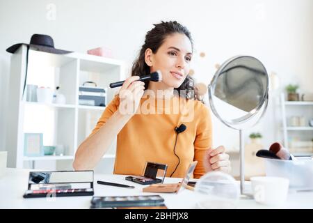 Beauty blogger applying contouring powder on her face using make-up brush, horizontal low angle shot Stock Photo