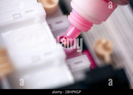 Bottle with magenta colour ink refilling printer cartridge. Closeup. Stock Photo