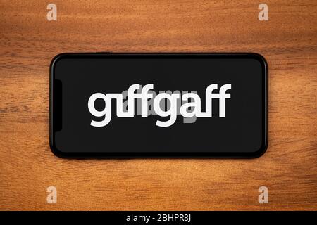 A smartphone showing the Giffgaff logo rests on a plain wooden table (Editorial use only). Stock Photo