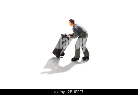 Miniature man pushing a black garbage bin or wheelie on a white background with drop shadow in a waste disposal concept Stock Photo
