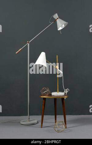 Two vintage anglepoise lamps, one a freestanding floor lamp and the second a table lamp on a stool , against a grey wall indoors Stock Photo