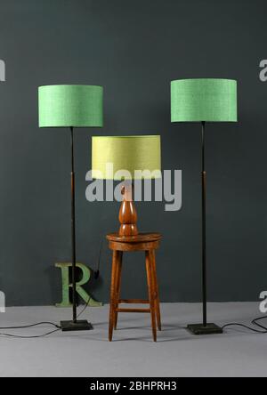 Three vintage lamps with green shades, two matching floor lamps flanking a wooden table lamp on a stool in a grey room in an interior decor concept Stock Photo