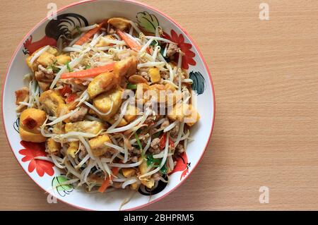 Stir fried bean sprouts with tofu, carrots, celery, ground pork, garlic, vegetable oil and a little chili. Placed on a plate on a wooden background. Stock Photo