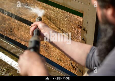 Unrecognizable man cleaning a wooden gate with a power washer. High water pressure cleaner  used to DIY repair garden gate. Stock Photo