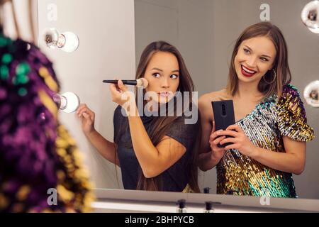 Two women putting on make up and looking in a mirror. Stock Photo