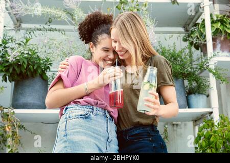 Two women standing close together having a drink on a terrace Stock Photo