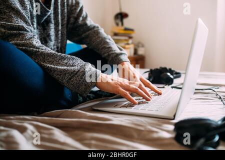 Close up of person sitting on bed, working on laptop computer during Corona virus crisis. Stock Photo