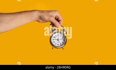 Meeting deadlines and scheduling. Millennial guy holding alarm clock on orange background, closeup. Copy space. Panorama Stock Photo