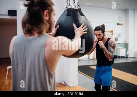 Rear view of a man steadying a small punchbag for a boxer to punch. Stock Photo