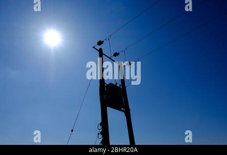 pole mounted overhead electricity transformer on blue sky background, norfolk, england Stock Photo