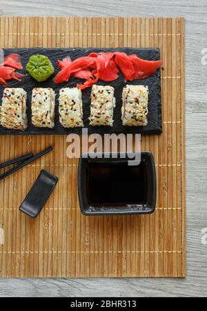 Originally laid out sushi roll on a black plate. With black chopsticks and soy sauce on a black plate Stock Photo