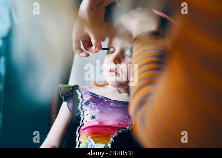 A girl sitting on a chair with her eyes closed as she has her face painted. Stock Photo