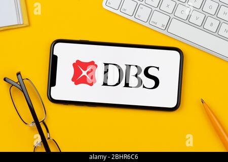 A smartphone showing the DBS Bank logo rests on a yellow background along with a keyboard, glasses, pen and book (Editorial use only). Stock Photo