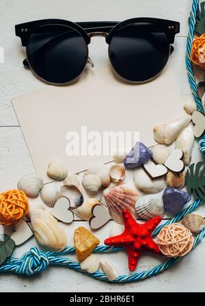 Different types of seashells, rope, sunglasses and blank sheet with place for text on wooden background Stock Photo