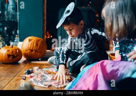 Two children sitting on a wooden floor looking at their sweets with pumpkins in the background. Stock Photo