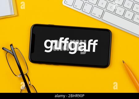 A smartphone showing the Giffgaff logo rests on a yellow background along with a keyboard, glasses, pen and book (Editorial use only). Stock Photo