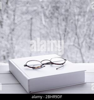 Round vintage reading glasses lie on a white thick notepad against the backdrop of the forest Stock Photo
