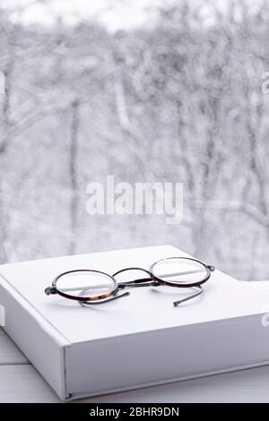 Round vintage reading glasses lie on a white thick notepad against the backdrop of the forest Stock Photo