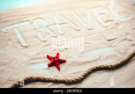 Mooring rope, seashells and red starfish on blue wooden table background. The inscription Travel is made on sand. Stock Photo