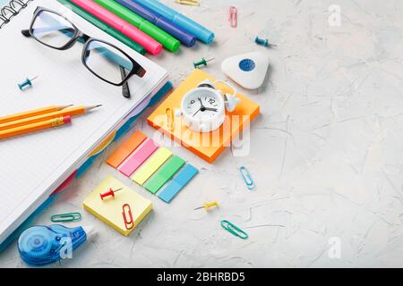 School stationery lies on a gray textural background with free space. The color of the rainbow, pencils, glasses, Notepad and Alarm clock remind you o Stock Photo