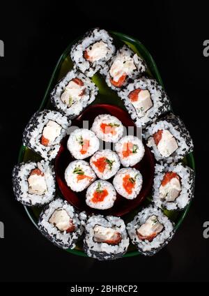 Japanese sushi food. Maki rolls and uramaki with tuna, salmon, caviar and cucumber. Sushi laid out in avocado shape on black background.