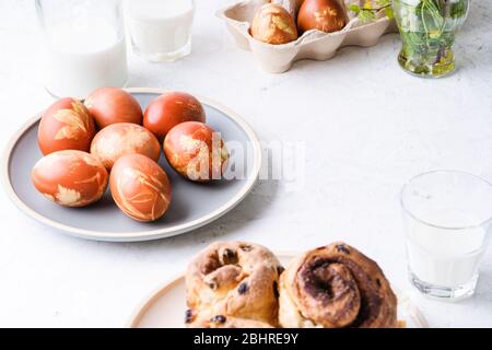 Easter brunch table. Cinnamon buns, naturally dyed with onion shells and springtime  plants Easter eggs in cardboard box, springtime  plants, zero was Stock Photo