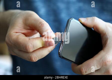Male hands getting sim card slot of his smartphone out Stock Photo