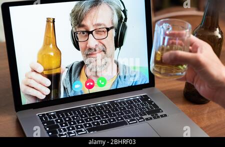 Video call between friends, distant relatives, middle-aged man toasts with beer together with another person using modern communication technologies Stock Photo