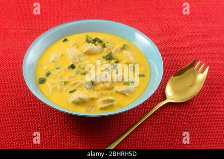 Chicken and vegetable chowder with chopped poblano peppers, corn, and onions in blue bowl with golden spork on red tablecloth Stock Photo