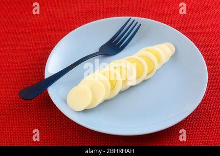 Hard boiled egg slices on blue breakfast plate with blue fork on red background Stock Photo