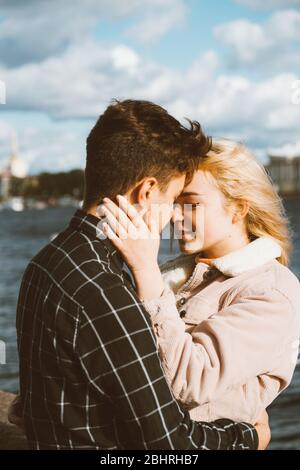 The boy looks tenderly at the girl and wants to kiss. A young couple stands embracing. The concept of teenage love and first kiss, sincere feelings of Stock Photo