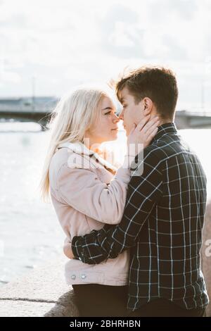 The boy looks tenderly at girl and wants to kiss. A young couple stands embracing. The concept of teenage love and first kiss, sincere feelings of man Stock Photo