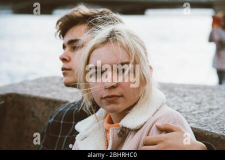 Teenagers in love sit on the waterfront in the city center, resting in autumn sun. Concept the first teenage love, the beginning of relations. A boy Stock Photo