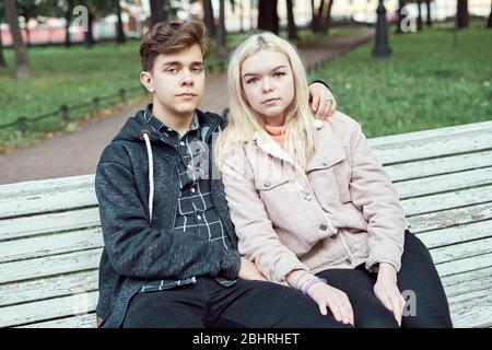 Teenagers in love sit on park bench in autumn, looking straight ahead. Concept of teen love Stock Photo