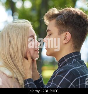 The boy looks tenderly at girl, hands clasped her face and wants to kiss. Concept of teenage love and first kiss Stock Photo