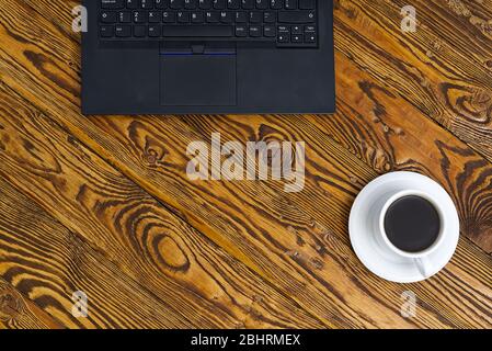 Laptop with cup of coffee on old brown wooden table. Top view to Notebook with cup of fresh coffee in home office in village. Stock Photo