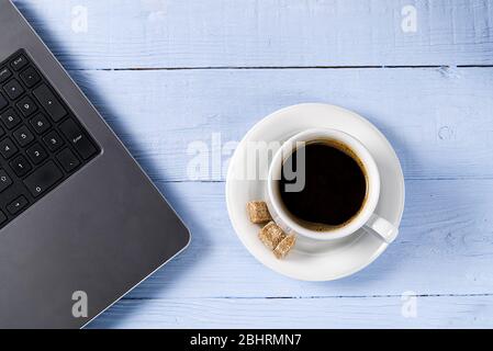 Laptop with cup of coffee on light blue old wooden table. Notebook with cup of fresh coffee in home office. Working from home concept Stock Photo