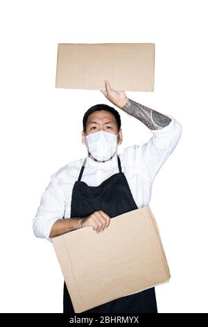 Bearded asian men waiter, chef dressed in black apron with medical mask is holding cardboard in white background.The concept of protest, attention, re Stock Photo