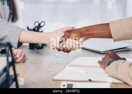 Cropped view of african american recruiter shaking hands with employee above table in office Stock Photo