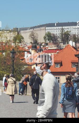 Prague, Czech Republic - April 23, 2020: People wearing medical face masks on the Charles Bridge. Old town in background. City center during coronavirus pandemic. COVID-19 crisis. Vertical photo.