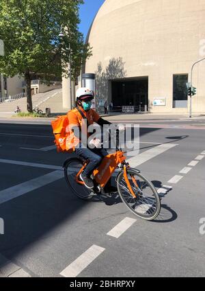 Cologne, Germany - 26 April 2020: A delivery man wearing a protective face mask delivers food during the lock-down days in Germany. Stock Photo