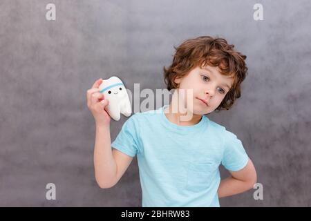 cute curly boy holds big tooth. The concept of children's health, medicine. Stock Photo