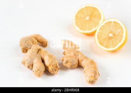 Closeup image of ingredients for natural cold or flu remedy includes ginger and lemon on a white wooden background. Selective focus on front slice of Stock Photo