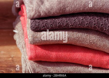 Stack of folded beige and pink clothes on brown wooden background. Female blouses pile. Stock Photo