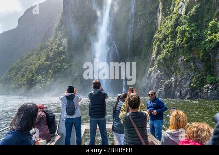 Milford Sound, New Zealand. Tourists photographing Stirling Falls from the deck of a cruise boat, Milford Sound, Fiordland National Park, New Zealand Stock Photo