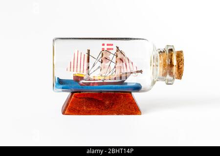 A tiny model sailing ship in a small glass bottle, sealed with a cork, isolated on a white background Stock Photo