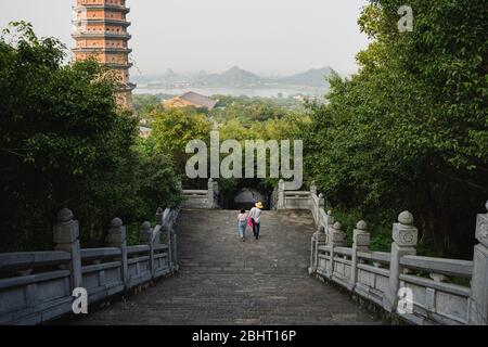 people going down the stairs between the trees in the Bai Dinh temple Stock Photo